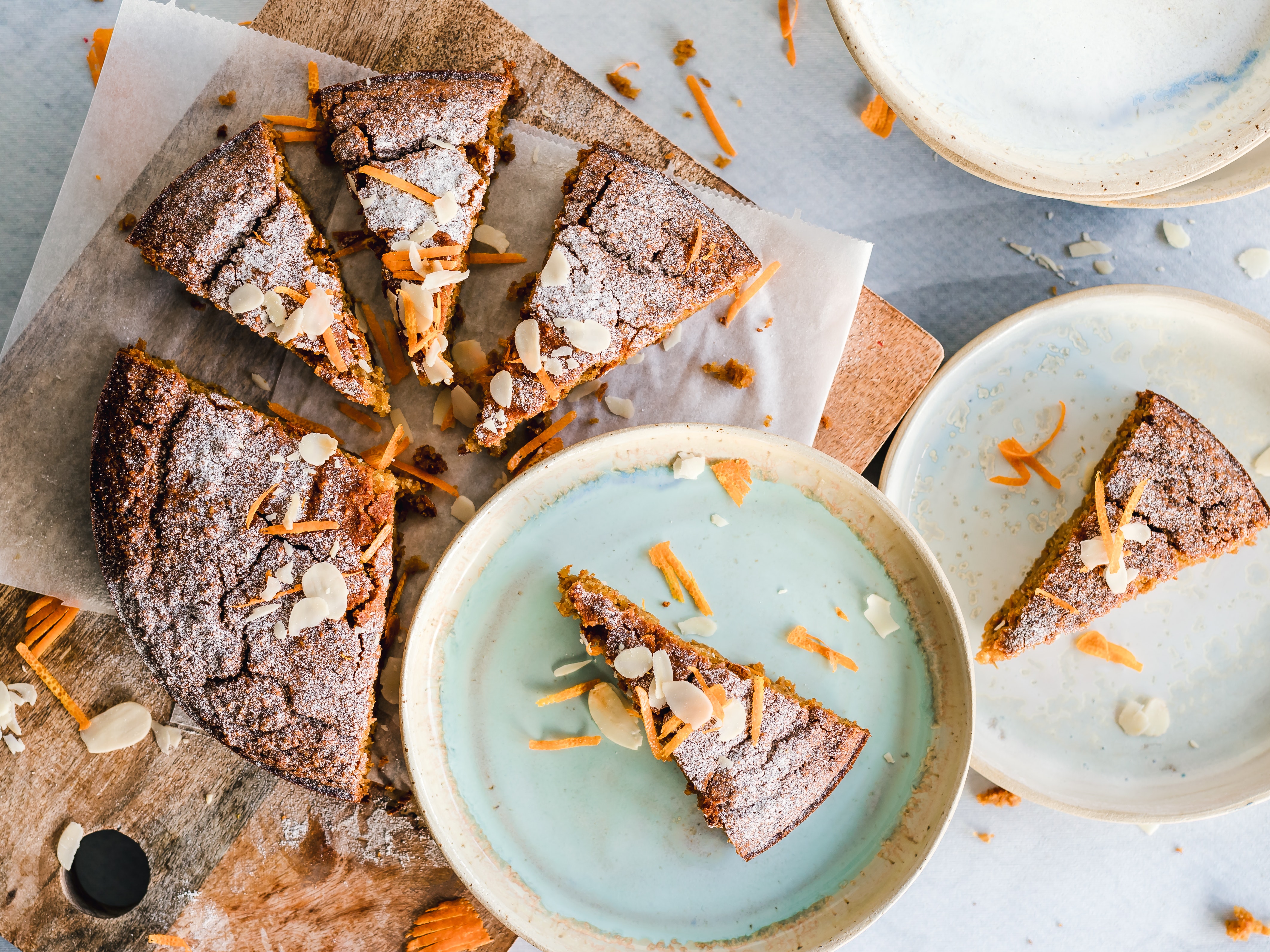 Carrot cake sprinkled with almond slices and grated carrot. Two slices of the cake are placed on plates. Cakes often contain gluten/